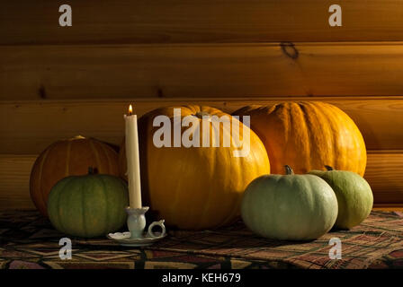 five different-colored pumpkins of different sizes and a candle in a vintage candlestick lie on a table covered with a cloth, against the background o Stock Photo