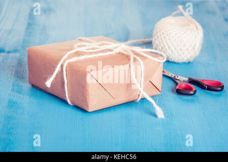 Homemade gift box wrapped with classic brown paper and tied with white string, scissors and twine in background Stock Photo
