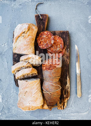 Wine snack set. Hungarian mangalica pork salami sausage and rustic bread on dark wooden board over a rough grey-blue concrete background, top view, ve Stock Photo