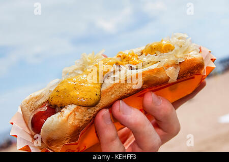 Hand holding hot dog with mustard and sauerkraut Stock Photo