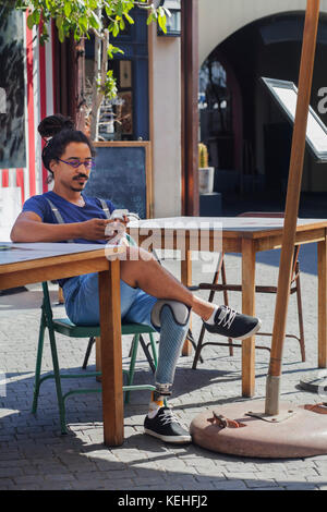 Mixed race man with prosthetic leg texting on cell phone at sidewalk cafe Stock Photo
