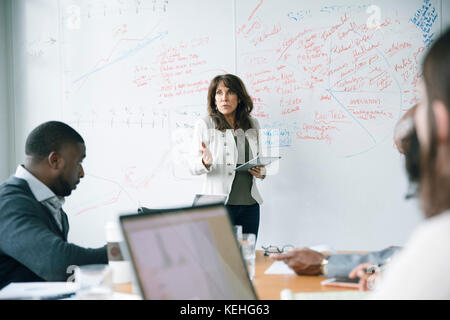 Businesswoman holding digital tablet near whiteboard in meeting Stock Photo