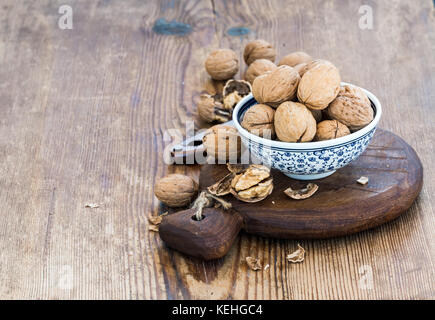 Walnuts in ceramic bowl and on wooden board with nutcracker over  rustic wooden background, selective focus Stock Photo