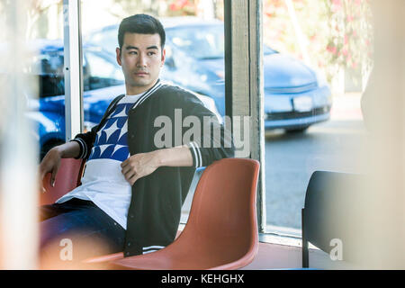 Serious Chinese man sitting in chair near window Stock Photo