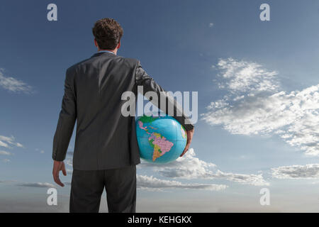 Caucasian businessman holding globe in sky Stock Photo