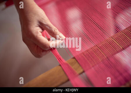 Hand of Hispanic woman weaving fabric on loom Stock Photo