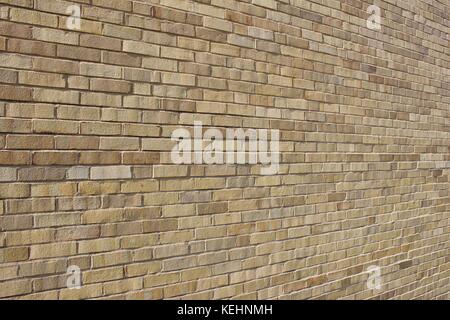 Close up angled view of a brightly sunlit beige and tan colored modern brick wall background. Stock Photo