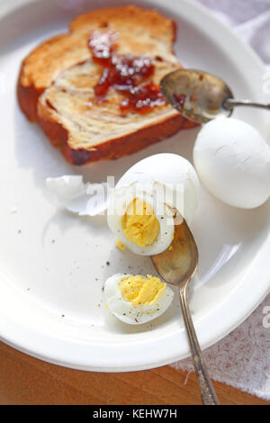 Partially peeled boiled and cracked eggs with cinnamon bread toast spread with strawberry jam Stock Photo
