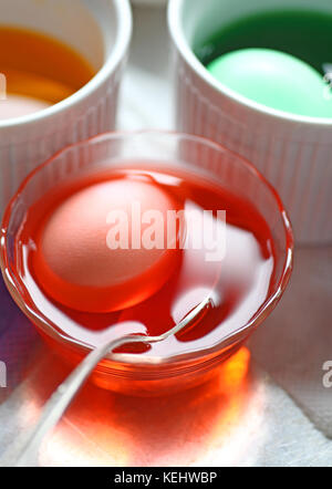 Eggs being dyed in green and orange colors in various dishes with spoon Stock Photo