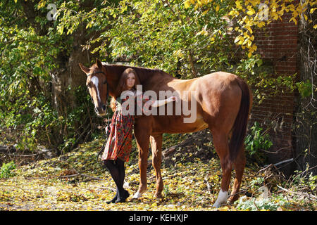 Young attractive red head woman leading her big horse down a country Stock Photo