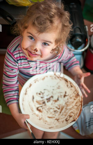 Young girl cleaning a chocolate bowl after making cake Stock Photo