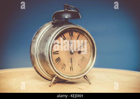 Vintage alarm clock on wooden table, blue background, deliberately grainy Stock Photo
