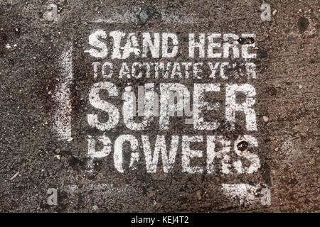 Stand Here to Activate Your Super Powers - spray-painted stencil on the sidewalk in NYC Stock Photo