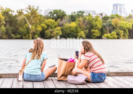 Washington DC, USA - August 4, 2017: Two girl friends university students sitting in Georgetown park harbor on riverfront in evening with potomac rive Stock Photo