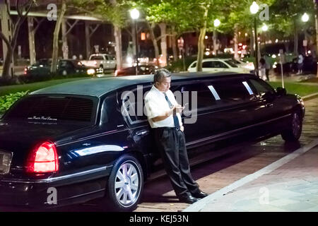 Washington DC, USA - August 4, 2017: Limo limousine driver standing by car sidewalk looking at mobile smartphone phone in Georgetown neighborhood duri Stock Photo
