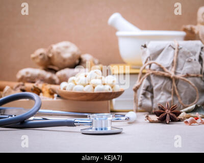 Alternative health care dried various Chinese herbs in wooden box lotus seed and saffron in wooden spoon on medical textbook with mortar on brown back Stock Photo