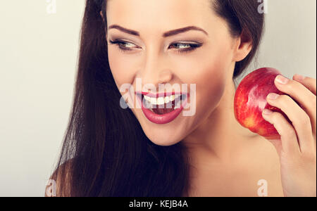 Beautiful excited makeup brunette woman holding red tasty apple and with open mouth looking on empty space. Closeup toned color portrait Stock Photo