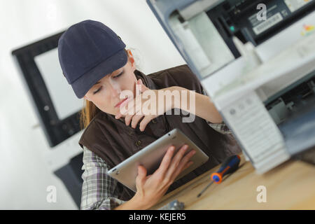 female mechanic using tablet to fix a printer Stock Photo