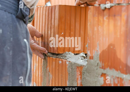 professional construction worker laying clay brick block and building wall in industrial site. Detail of hands adjusting bricks Stock Photo