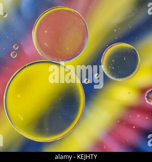 A macro shot of oil floating on water above a colourful background of coloured pencils. Stock Photo