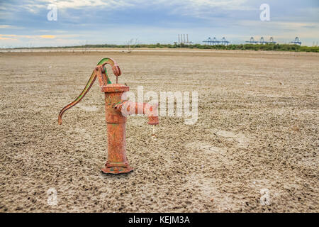Rusty water pump on land with dry and cracked ground. Desert Stock Photo