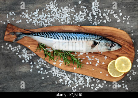 Mackerel fish health food on an olive wood board with course salt, rosemary herb and lemon fruit on marble background. High in omega 3 .