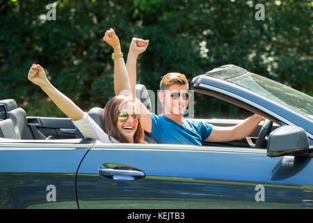 Happy Couple Sitting In A Car Wearing Sunglasses Raising Their Arms Stock Photo