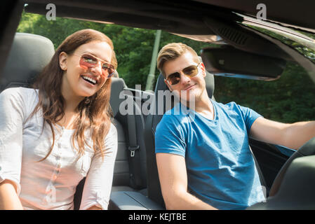 Portrait Of Smiling Young Couple In A Car Wearing Sunglasses Stock Photo