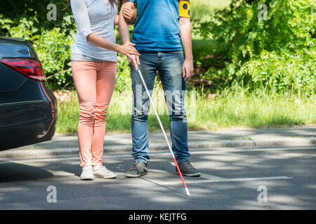 Woman Assisting Blind Man With White Stick On Street Stock Photo
