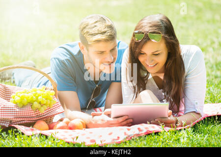Happy Couple Using Digital Tablet While Lying In Park Stock Photo