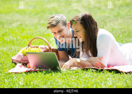 Happy Couple Using Laptop While Lying In Park Stock Photo