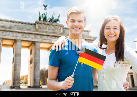 Smiling Young Couple Holding Flag At Brandenburg Gate Stock Photo