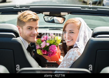 Young Smiling Just Married Couple With Bouquet In The Car Stock Photo