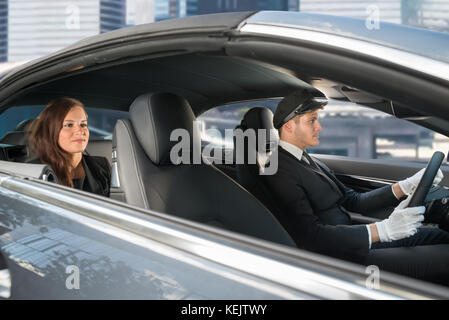 Beautiful Young Woman Traveling In A Car With Male Handsome Chauffeur Stock Photo