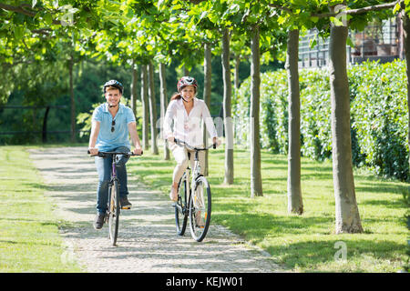 Young Smiling Couple Wearing Helmets On Theirs Heads Riding On The Bicycles In Park Stock Photo