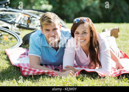 Two Young Happy Couple Laying Down On Green Grass At Park On Summer Day Stock Photo