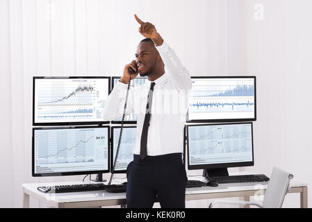 Male Stock Trader Pointing Upwards While Talking On Telephone Stock Photo