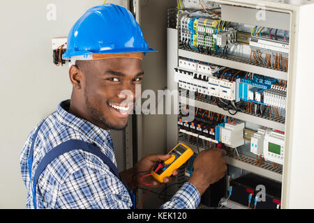 Young African Male Technician Examining Fusebox With Multimeter Probe Stock Photo