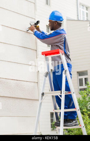 Young Happy Male Technician On Ladder Repairing Surveillance Camera Stock Photo