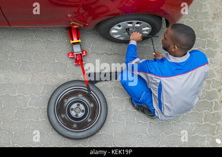 Young African Mechanic Changing Tire Of A Car With Wrench Stock Photo