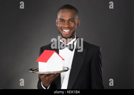 Young Happy Waiter Holding House Model In Tray Stock Photo