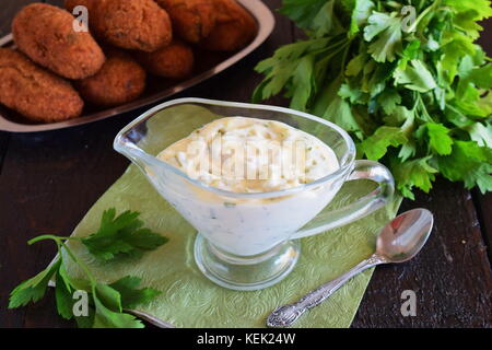 Tartar sauce for fish dishes with yogurt, capers, garlic and lemon, olive oil and sugar in a glass gravy boat on a dark wooden background. Healthy eat Stock Photo