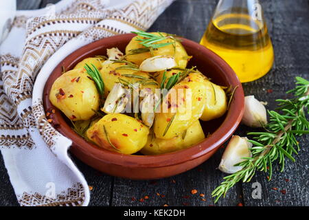 Oven cooked potato with rosemary, garlic, olive oil and mix of spices in a traditional ceramic bowl. Mediterranean lifestyle. Healthy eating concept. Stock Photo