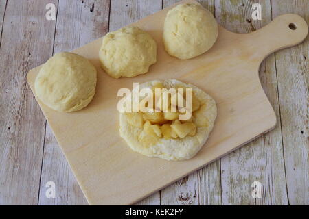 Homemade apple pies on a wooden cutting board. Dough with apple filling. Step by step cooking Stock Photo