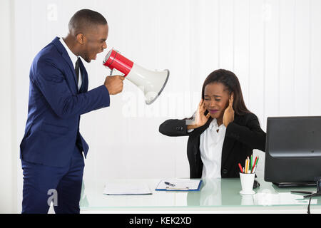 Boss Shouting At Young Businesswoman Through Loudspeaker In Office Stock Photo