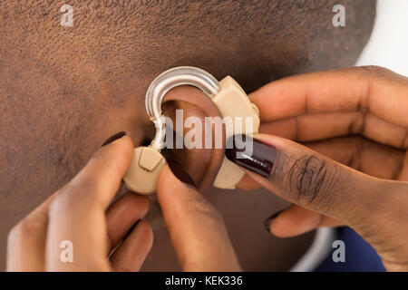 Close-up Of Doctor's Hand Inserting A Hearing Aid Into A Man's Ear Stock Photo