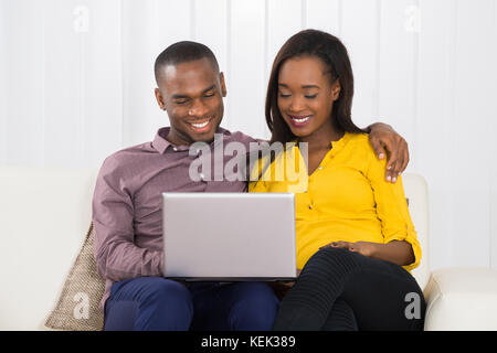 Happy Young Couple Sitting On Couch Using Laptop Stock Photo