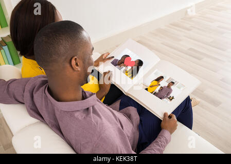 Couple Sitting On Sofa Looking At Photo Album Stock Photo