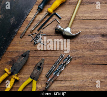 Rusty and old used carpentry and garage tools on a light brown wood background, showing varied tools,with metal pliers and saw,metal drill bits,hammer Stock Photo