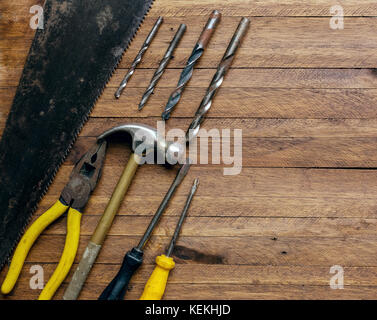 Rusty and old used carpentry and garage tools on a light brown wood background, showing varied tools,with metal pliers and saw,metal drill bits,hammer Stock Photo